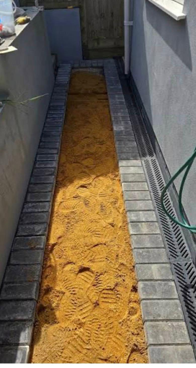 Before: a narrow side passage with a bare strip of loose sand between block edging